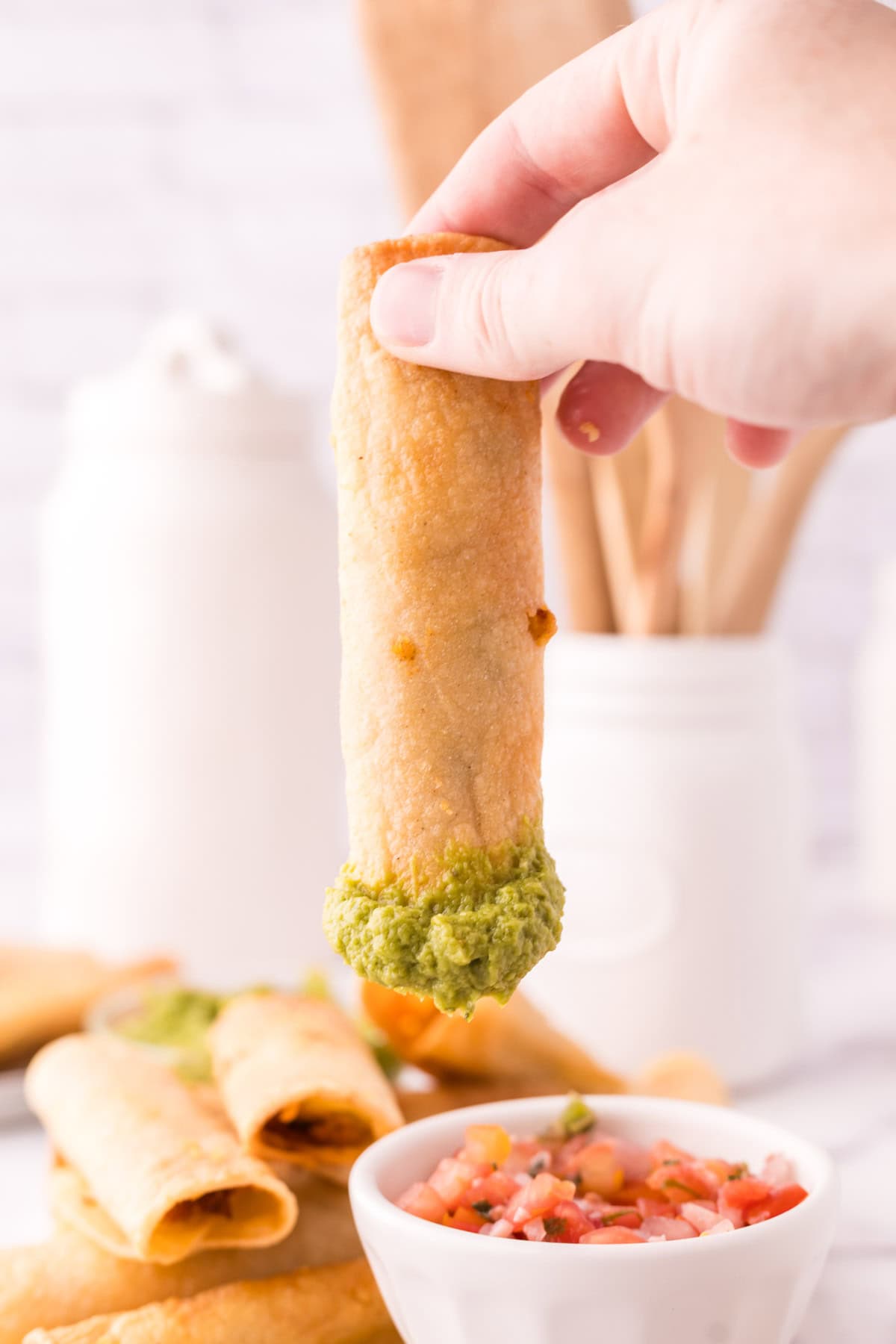 hand holding a taquito that is dipped in guacamole. 