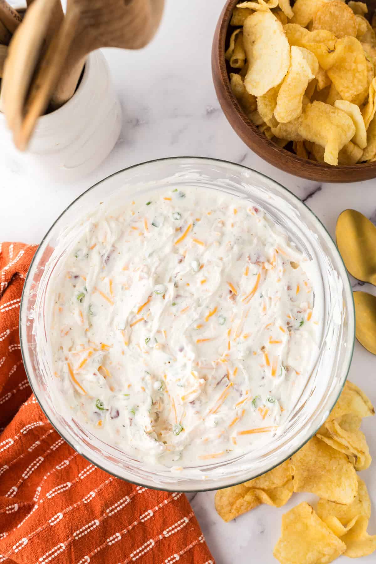loaded baked potato dip in a clear mixing bowl with potato chips.