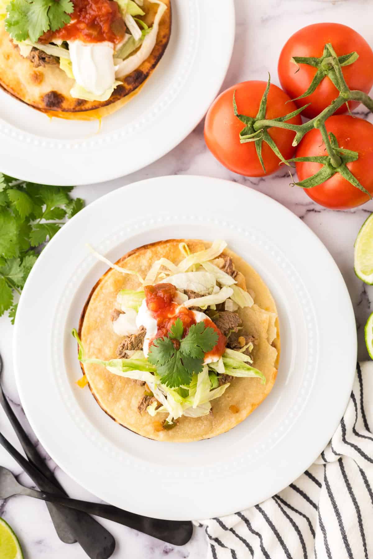 Mexican beef tostado on a round white plate with limes and cilantro.