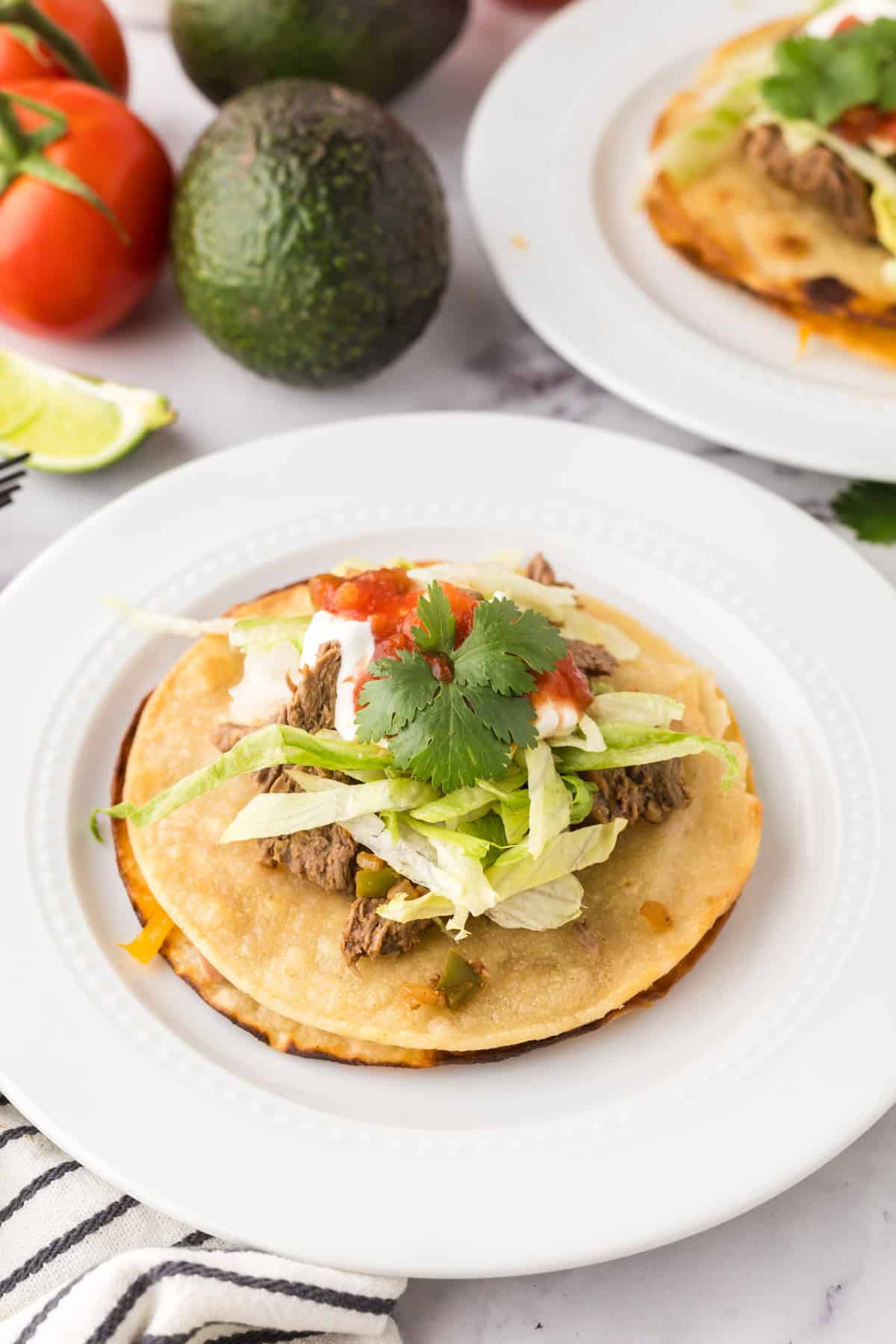 Mexican beef tostado on a round white plate with limes and cilantro.