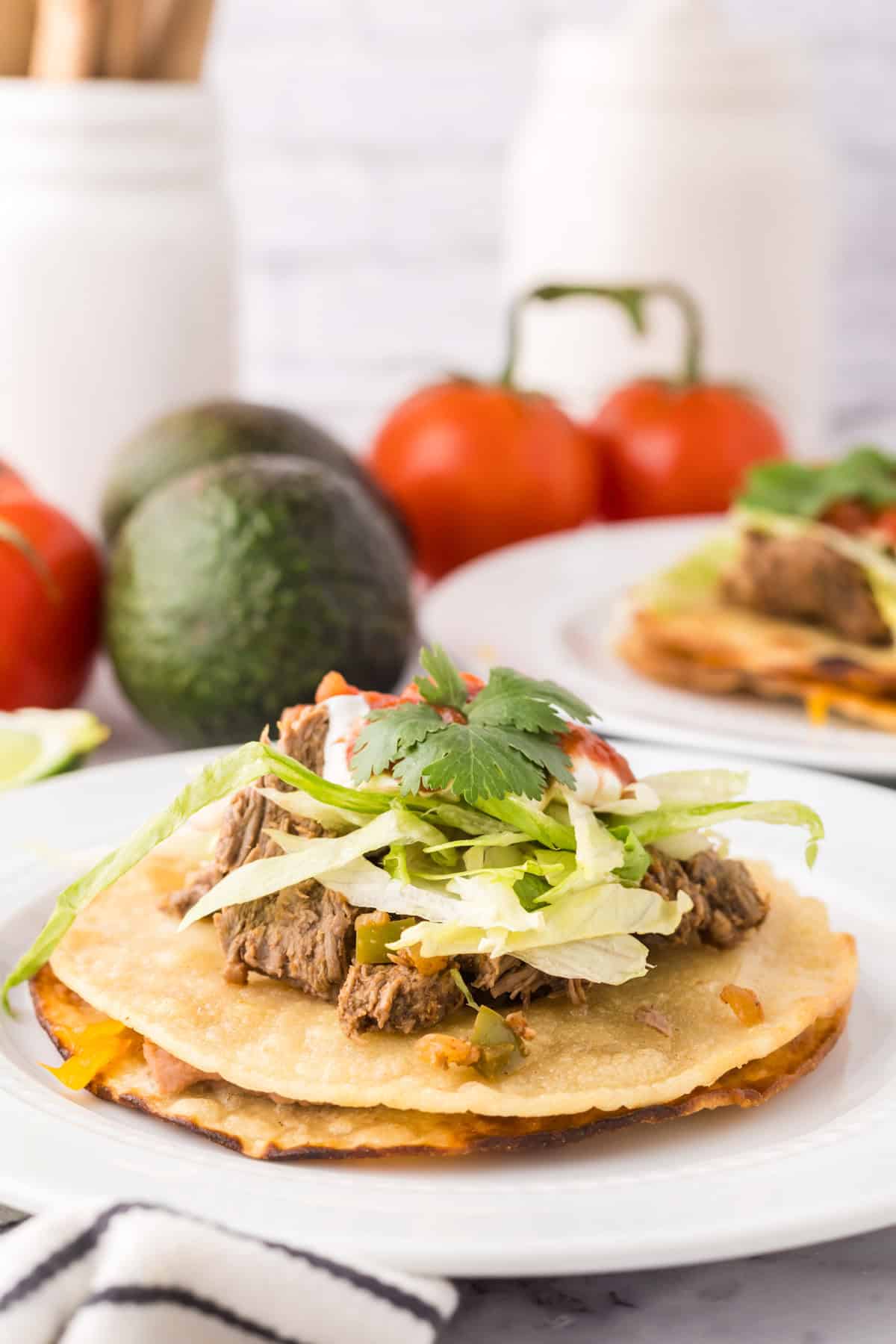 Mexican beef tostado on a round white plate with limes and cilantro.