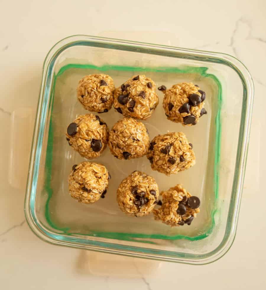9 completed no-bake oatmeal energy balls in a clear glass square container without the lid on.
