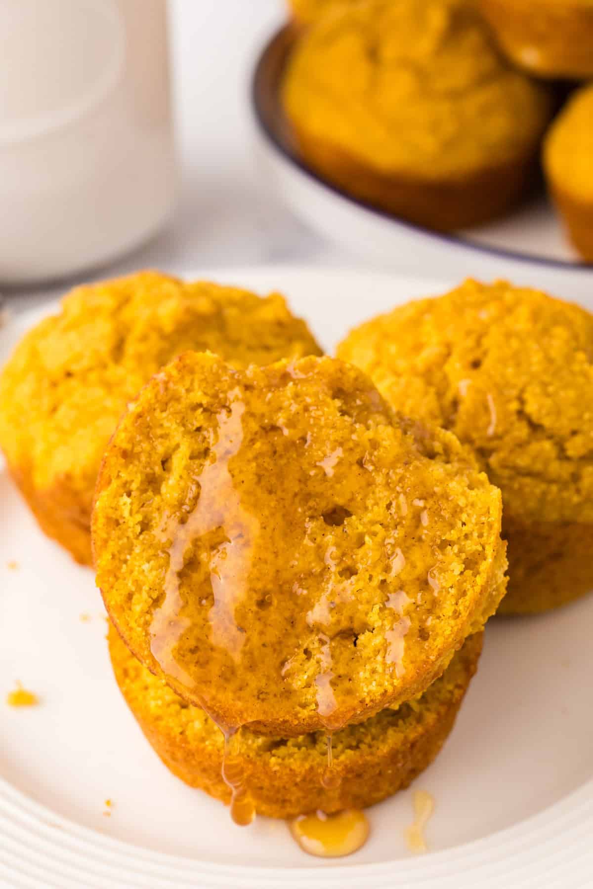 pumpkin cornbread muffins stacked on a round plate with honey on top.