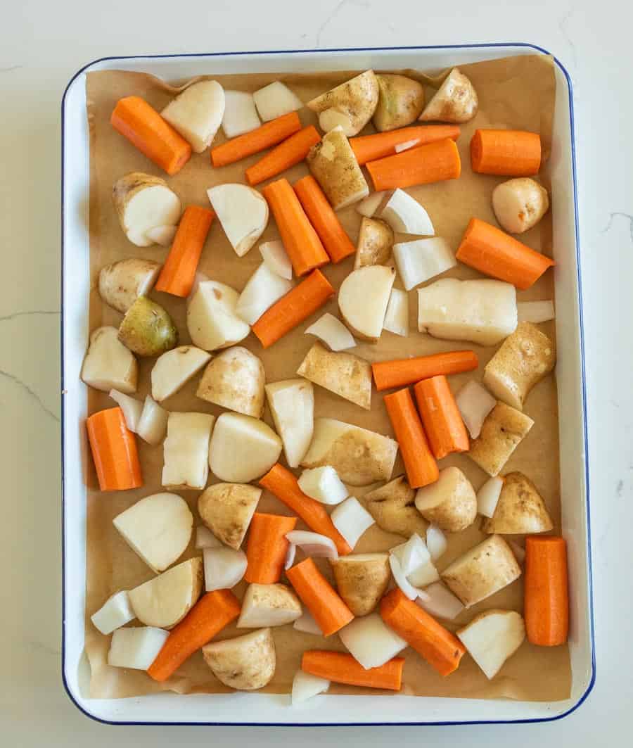 Raw potatoes, carrots, and onions on a lined sheet pan ready to bake.