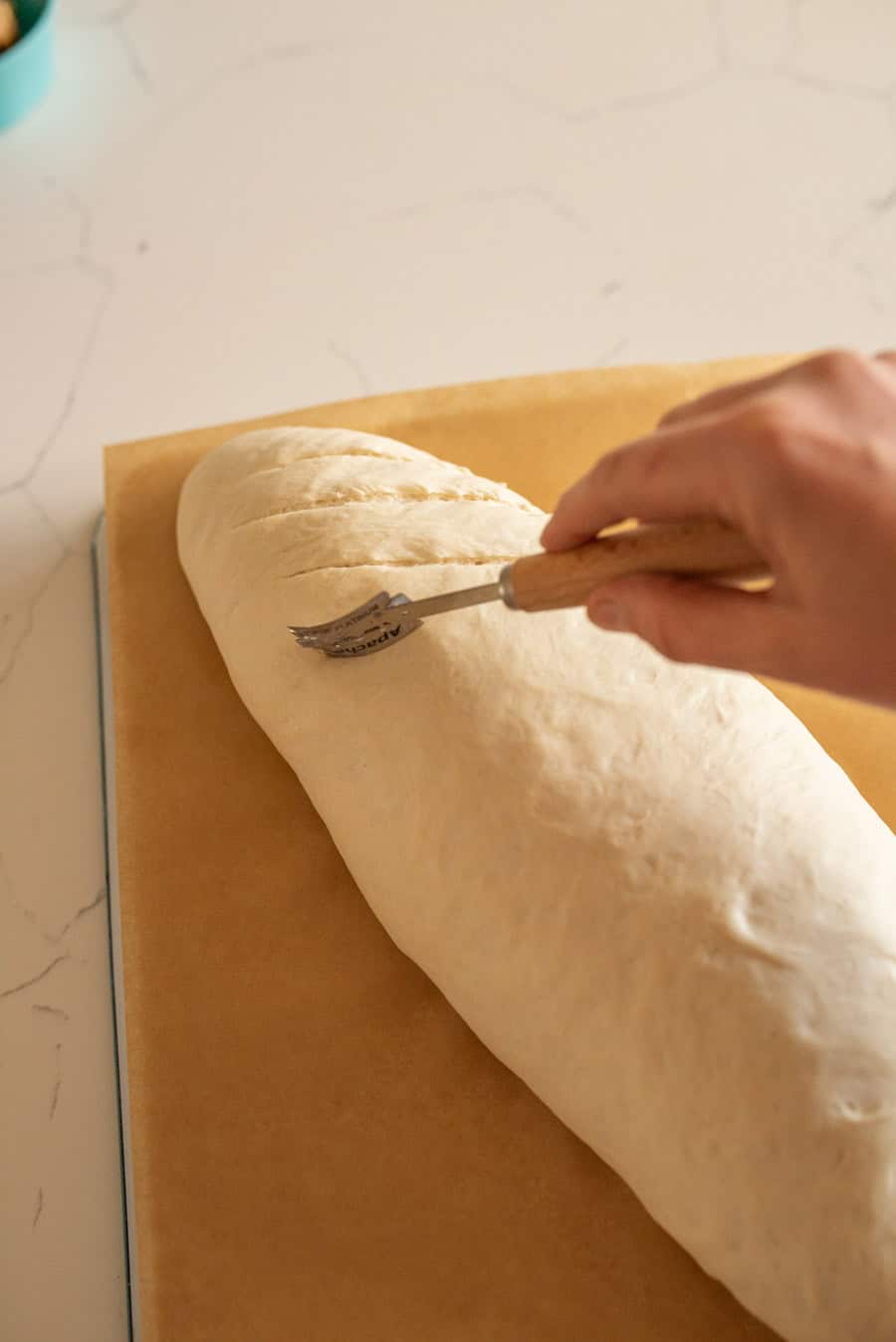Italian bread dough on a piece of brown parchment paper being scored after rising and before baking. 