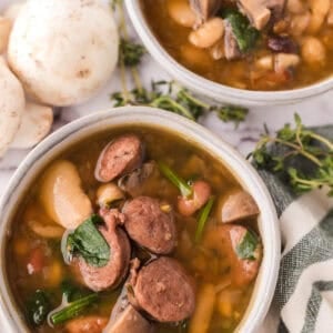 Sausage bean soup with spinach in white serving bowls.