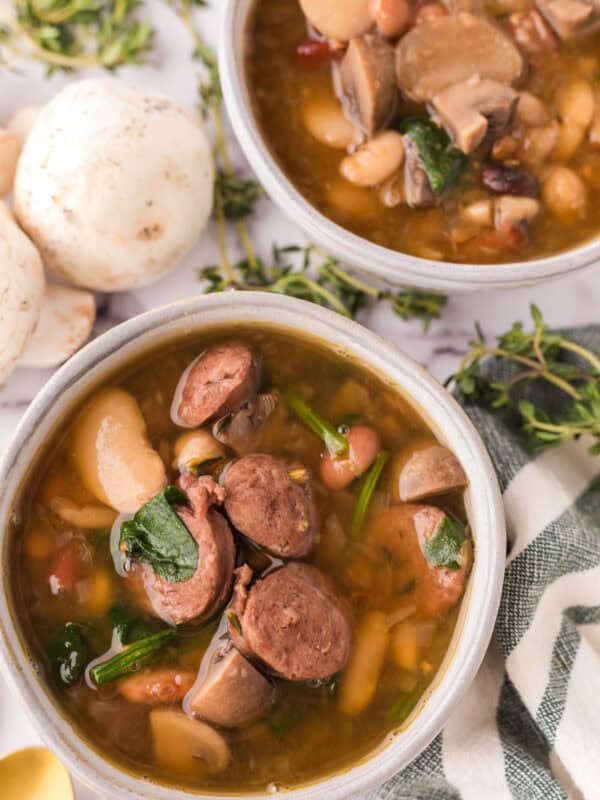 Sausage bean soup with spinach in white serving bowls.