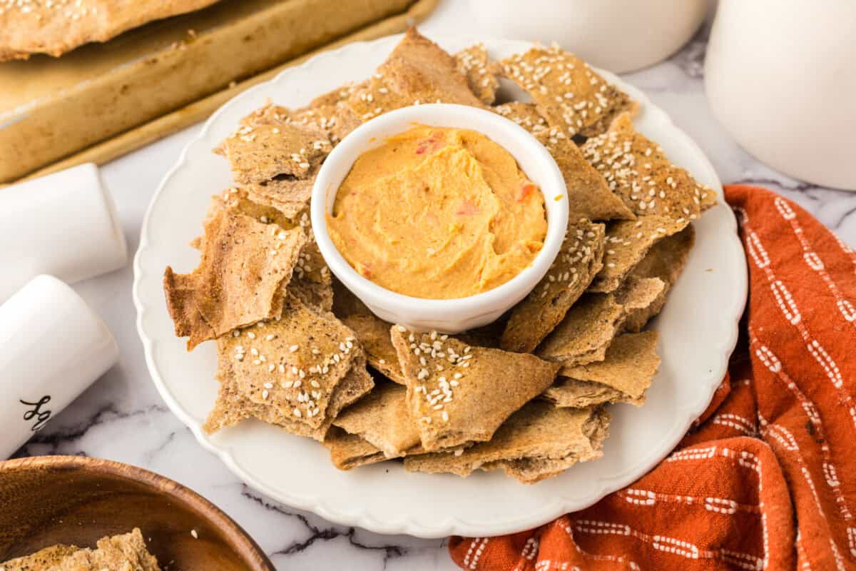 simple lavish bread crackers on a round plate with a bowl of dip in the middle.