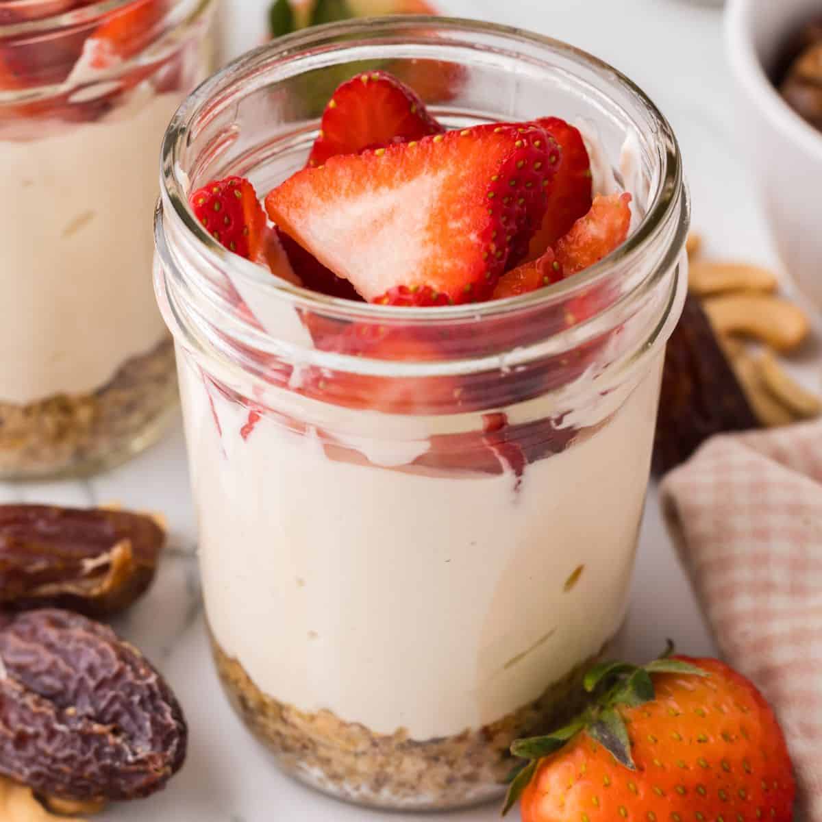 healthy no bake cheesecake with strawberries on top made inside a mason jar.