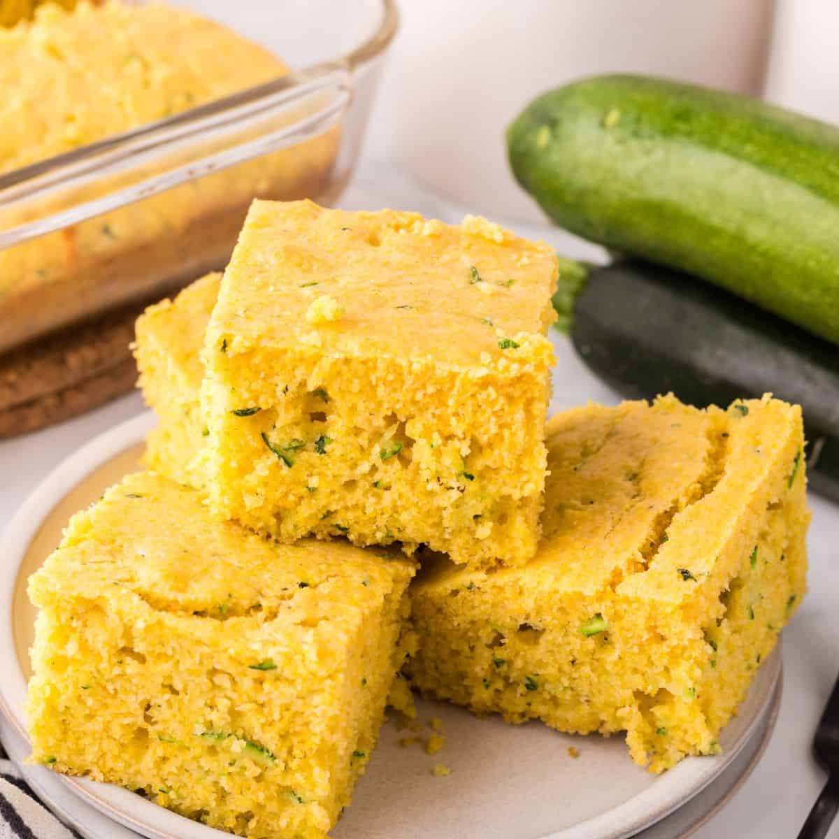 zucchini cornbread squares stacked on a plate.