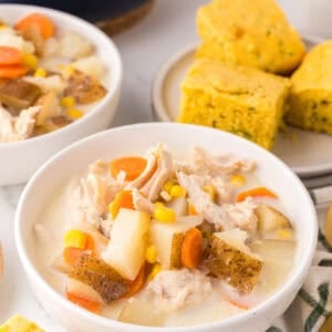 two white serving bowls of baked potato corn chowder next to zucchini cornbread.