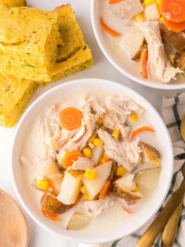 two white serving bowls of baked potato corn chowder next to zucchini cornbread.