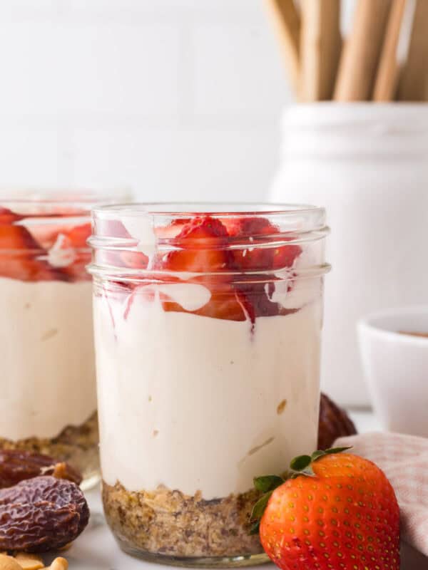 healthy no-bake cheesecake layered into a wide mouthed mason jar with fresh strawberries on top.