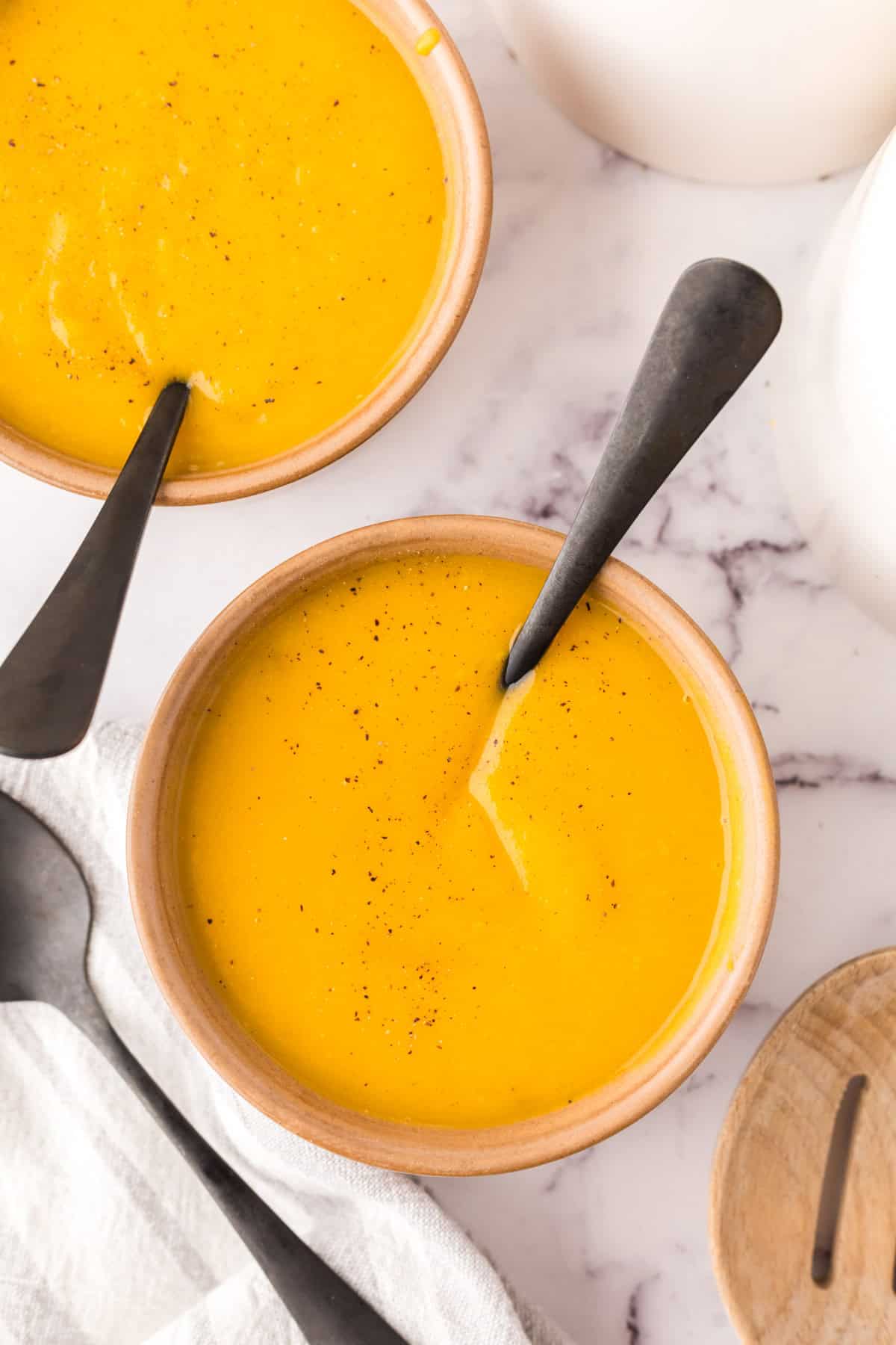 homemade butternut squash soup in two serving bowls with a black spoon in each.