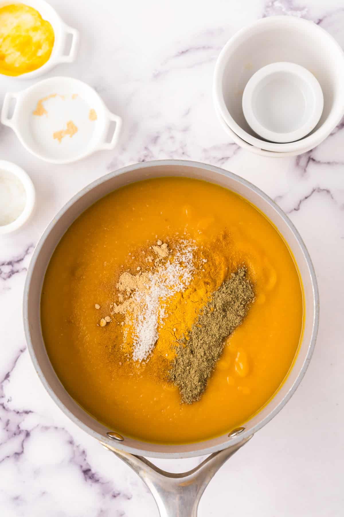 homemade butternut squash soup in progress in a sauce pan with spices being added.