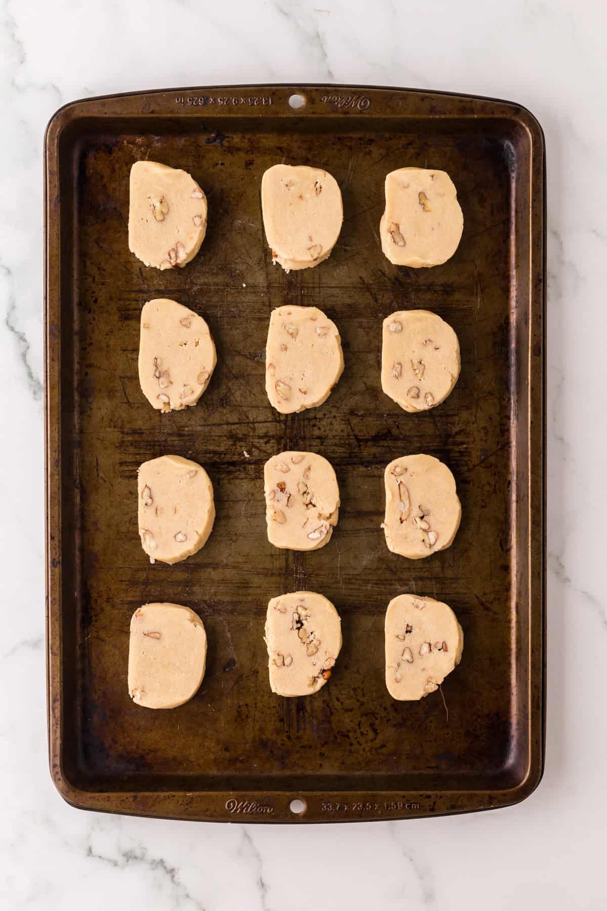 baking cookie sheet with sliced dough shapes of honey pecan cookies before going in the oven.