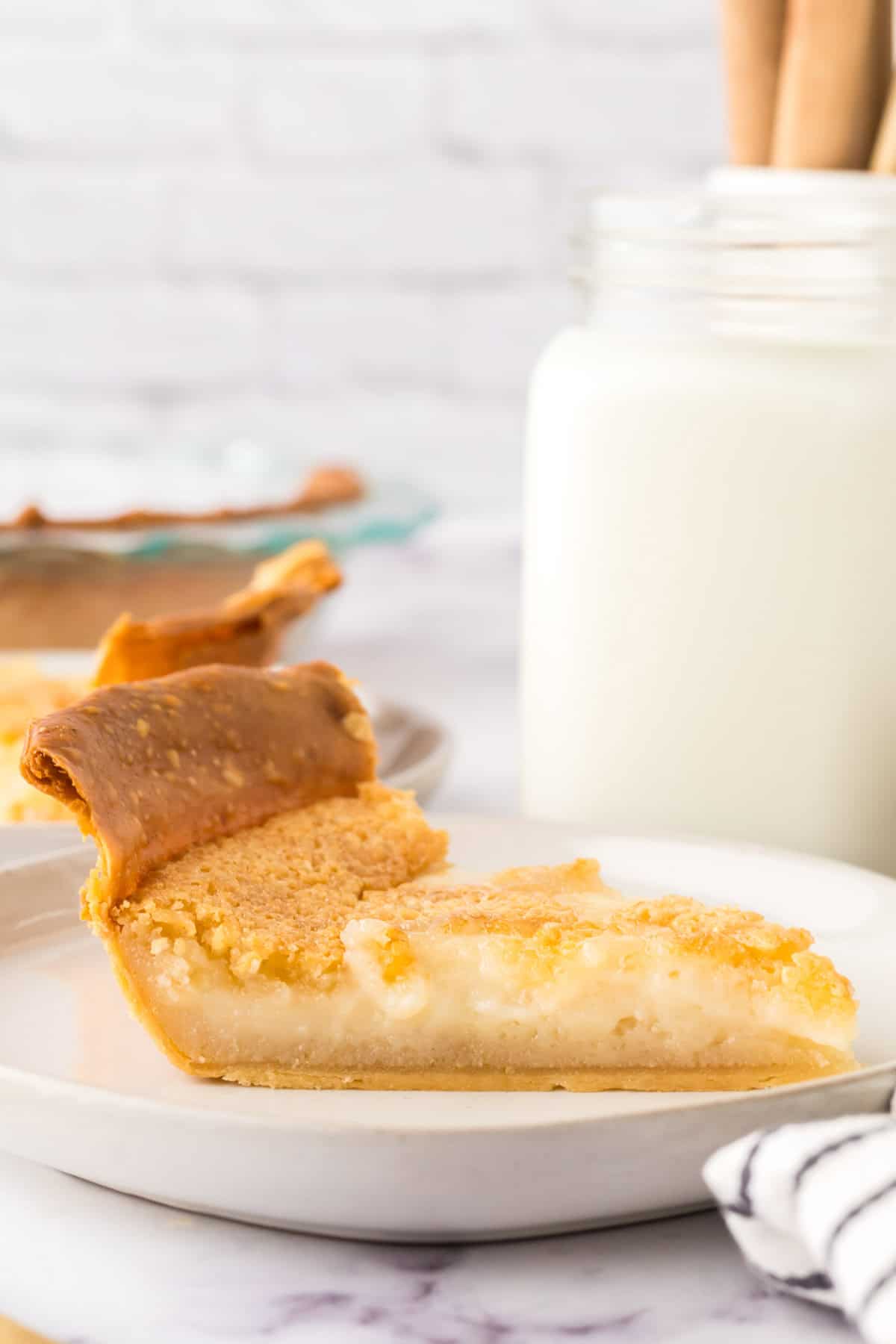 hoosier sugar cream pie slice on a round white plate next to a glass of milk.