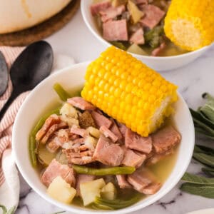 One pot farmstead wonder recipe served in a white bowl with corn on top next to black spoons.