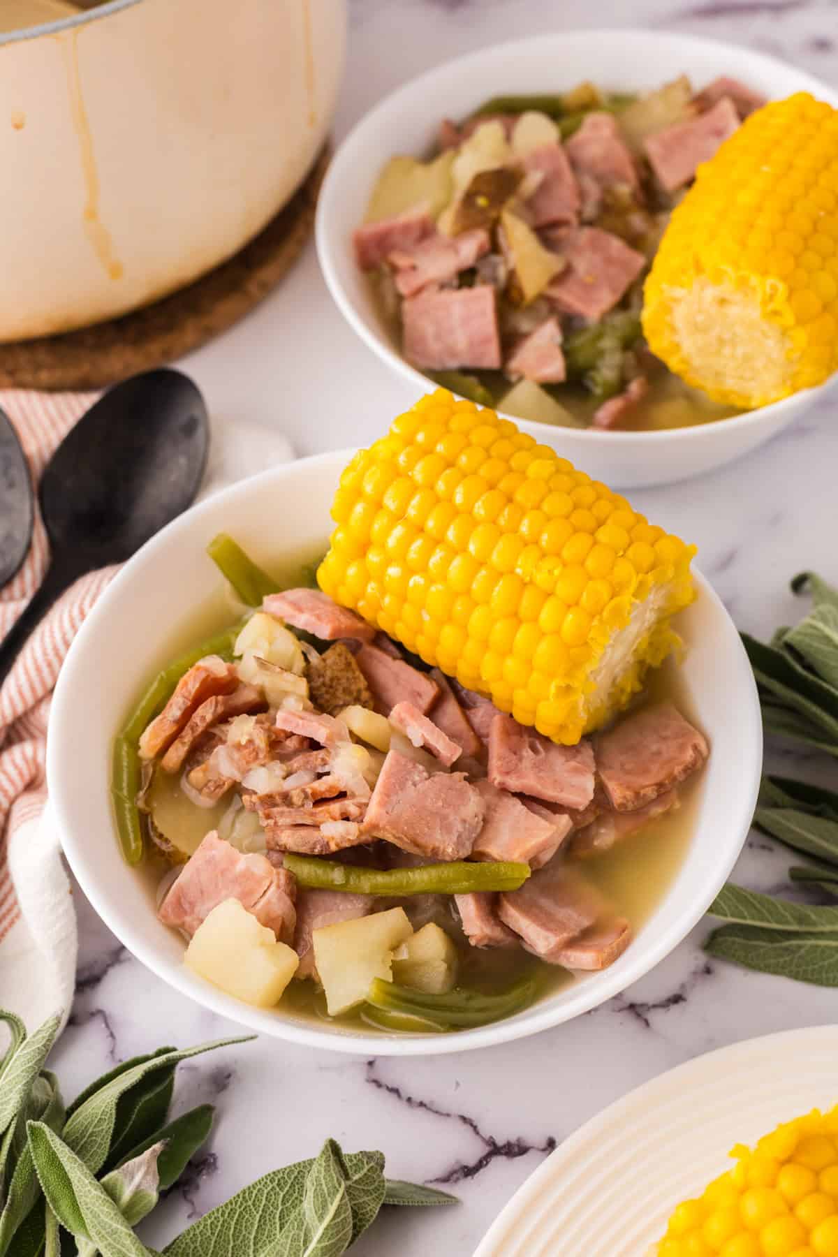 One pot farmstead wonder recipe served in a white bowl with corn on top next to black spoons.