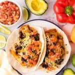 shrimp fajitas served over flour tortillas on a plate with fresh veggies all around.