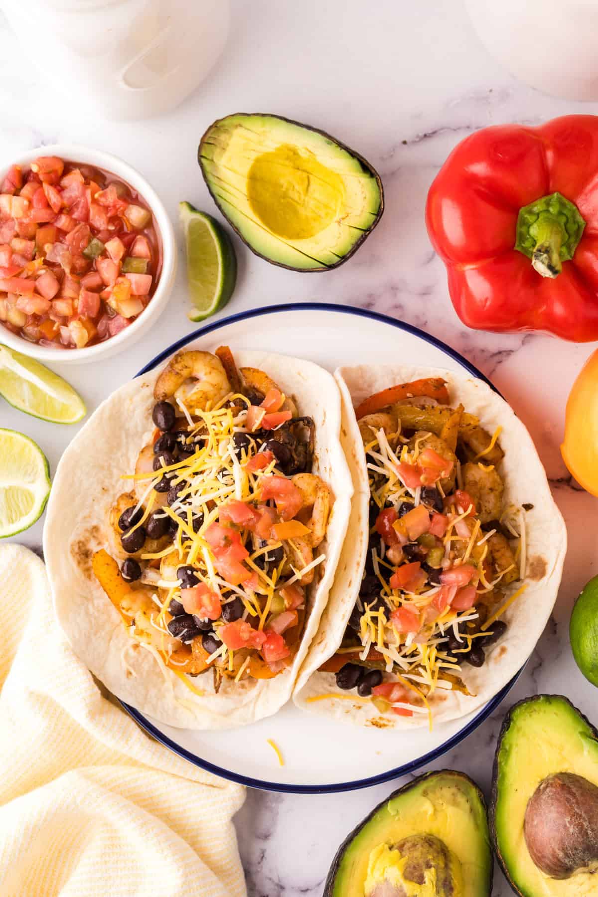 shrimp fajitas served over flour tortillas on a plate with fresh veggies all around.