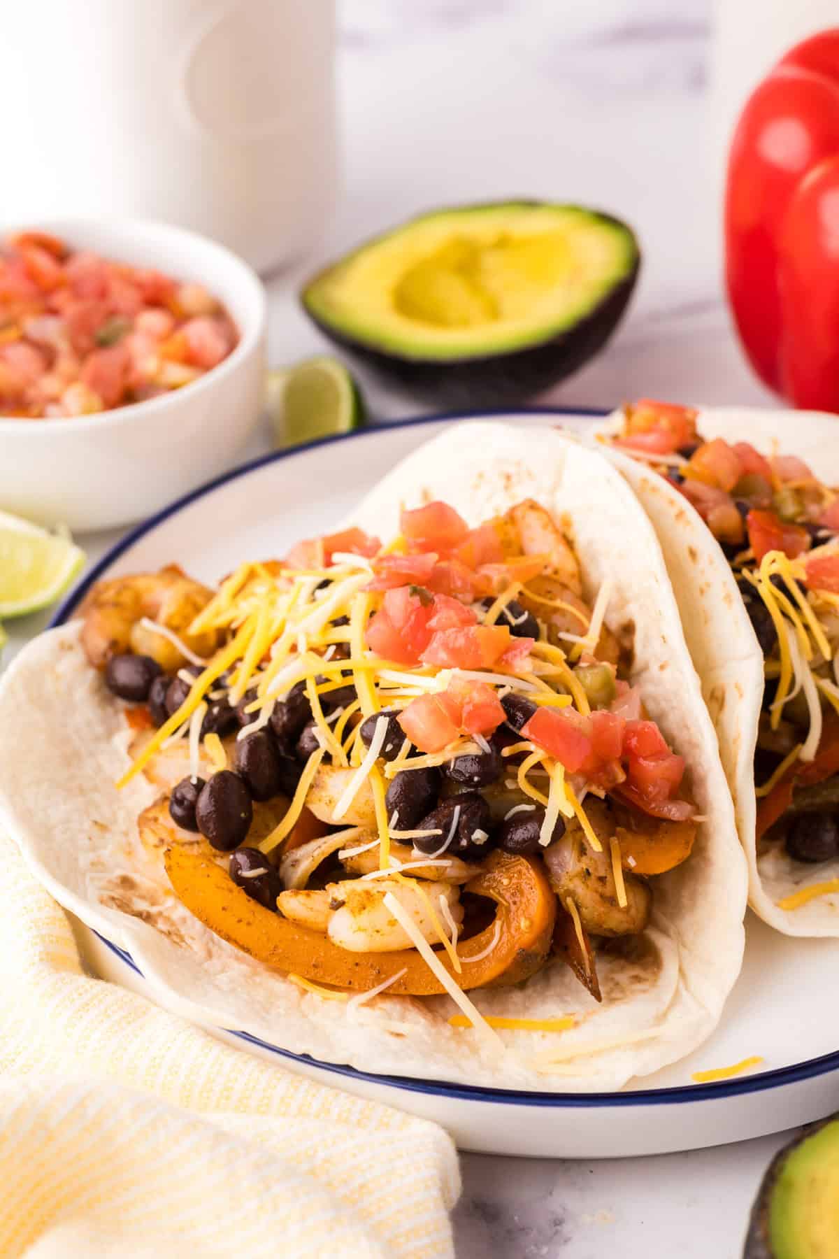 shrimp fajitas served over flour tortillas on a plate with fresh veggies all around.