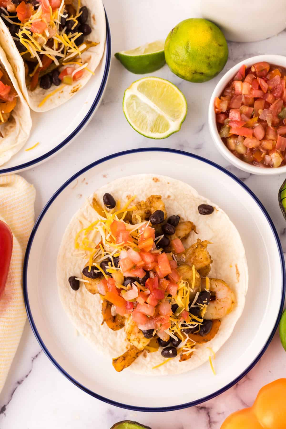 shrimp fajitas served over flour tortillas on a plate with fresh veggies all around.