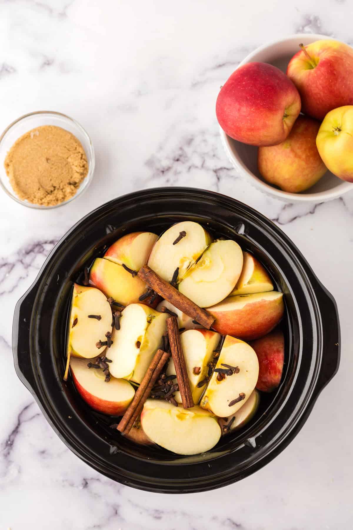 crock pot bowl filled with raw ingredients to make slow cooker apple cider.