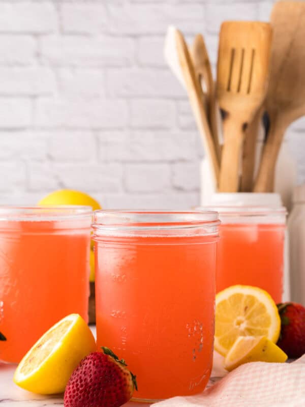 mason jars filled with fresh strawberry rhubarb lemonade with lemons al around.