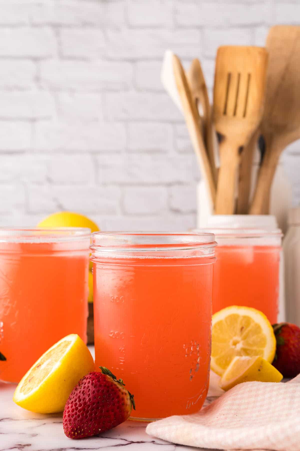 mason jars filled with fresh strawberry rhubarb lemonade with lemons al around.