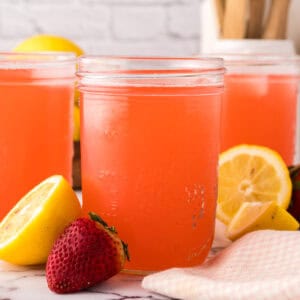 mason jars filled with fresh strawberry rhubarb lemonade with lemons al around.