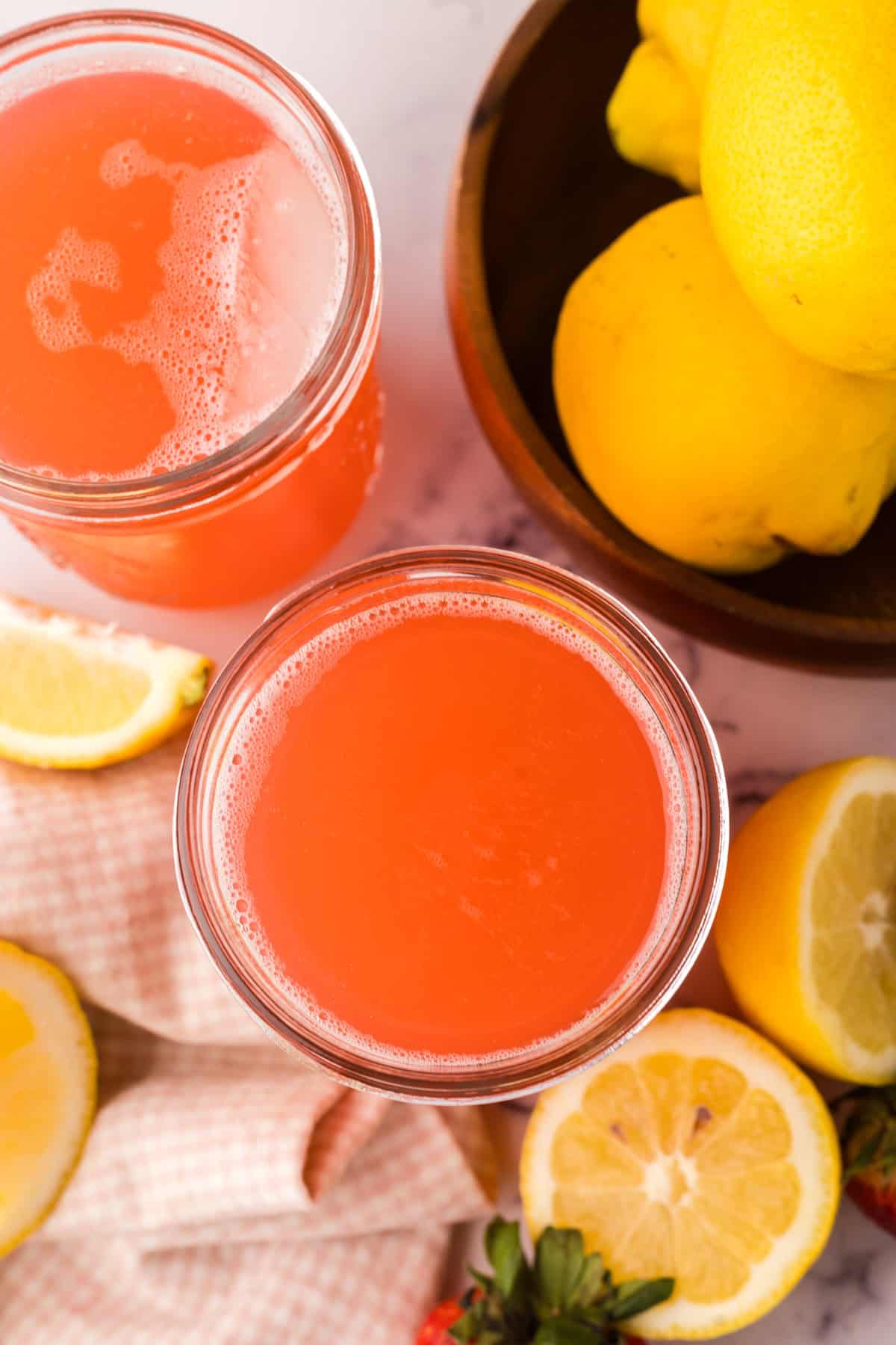 mason jars filled with fresh strawberry rhubarb lemonade with lemons al around.