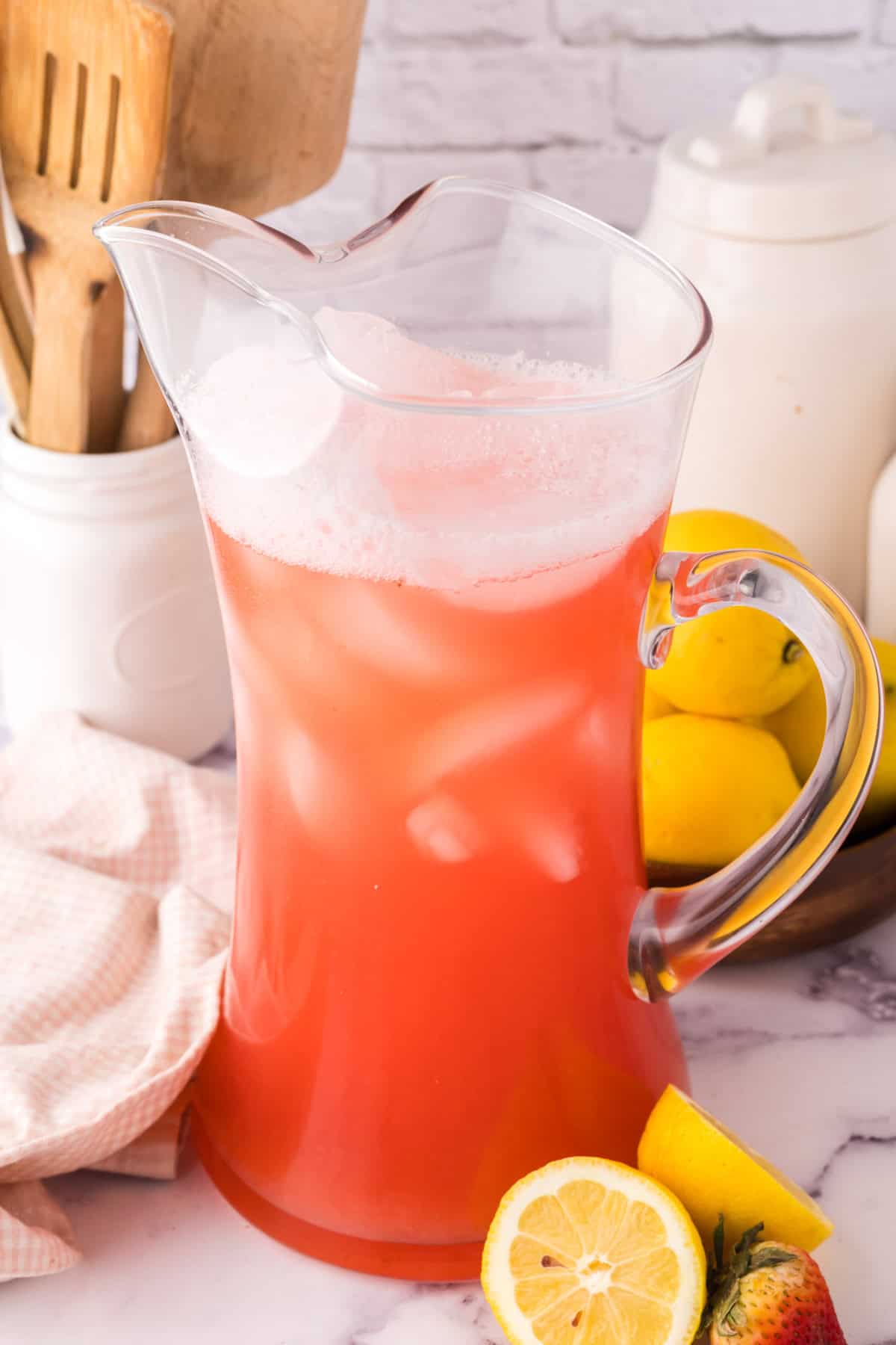 tall glass pitcher filled with ice and fresh strawberry rhubarb lemonade.