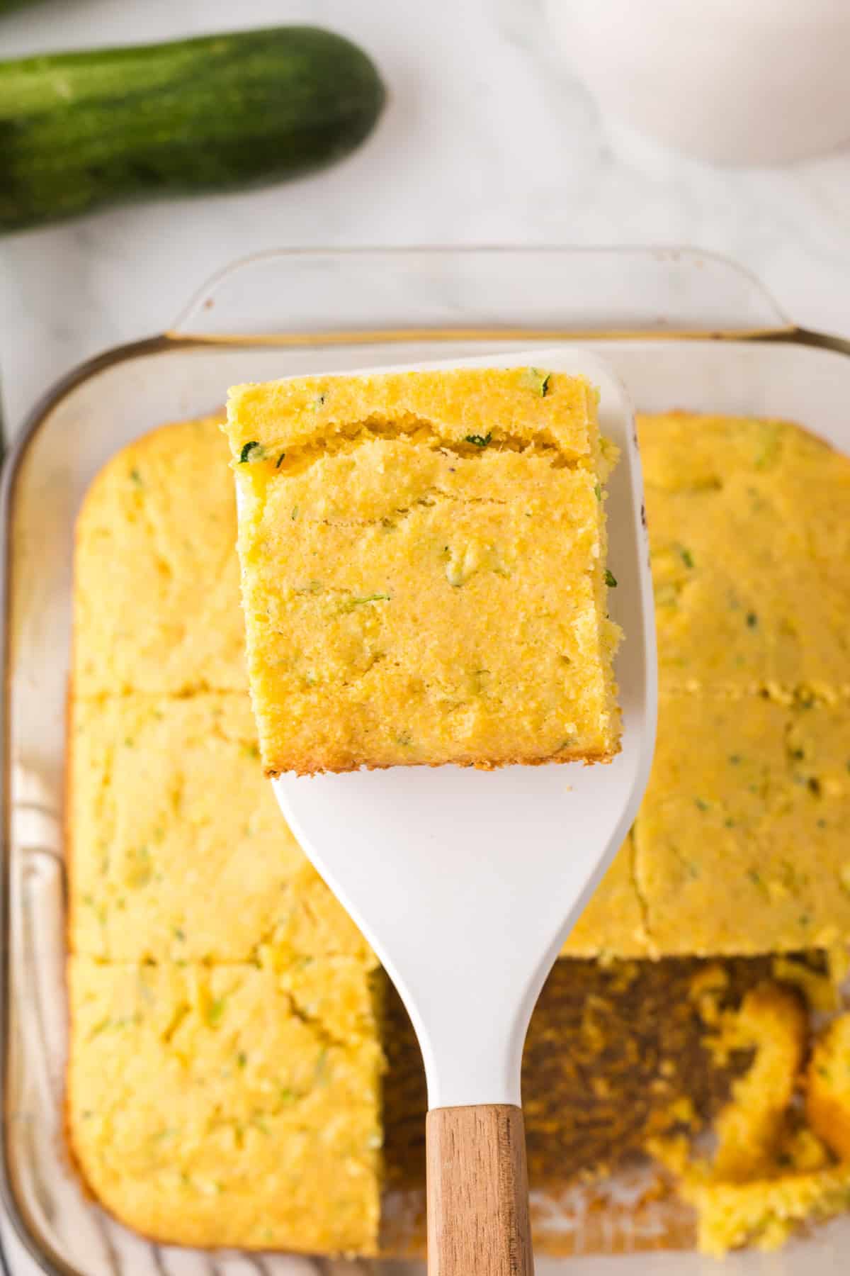 spatula holding a square slice of zucchini cornbread over the baking dish.