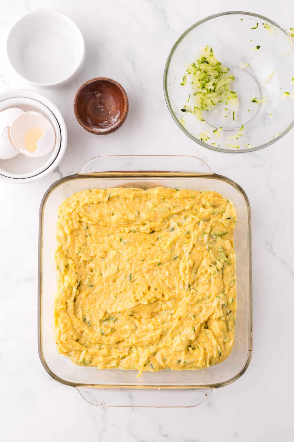 clear square baking dish with raw zucchini cornbread batter.