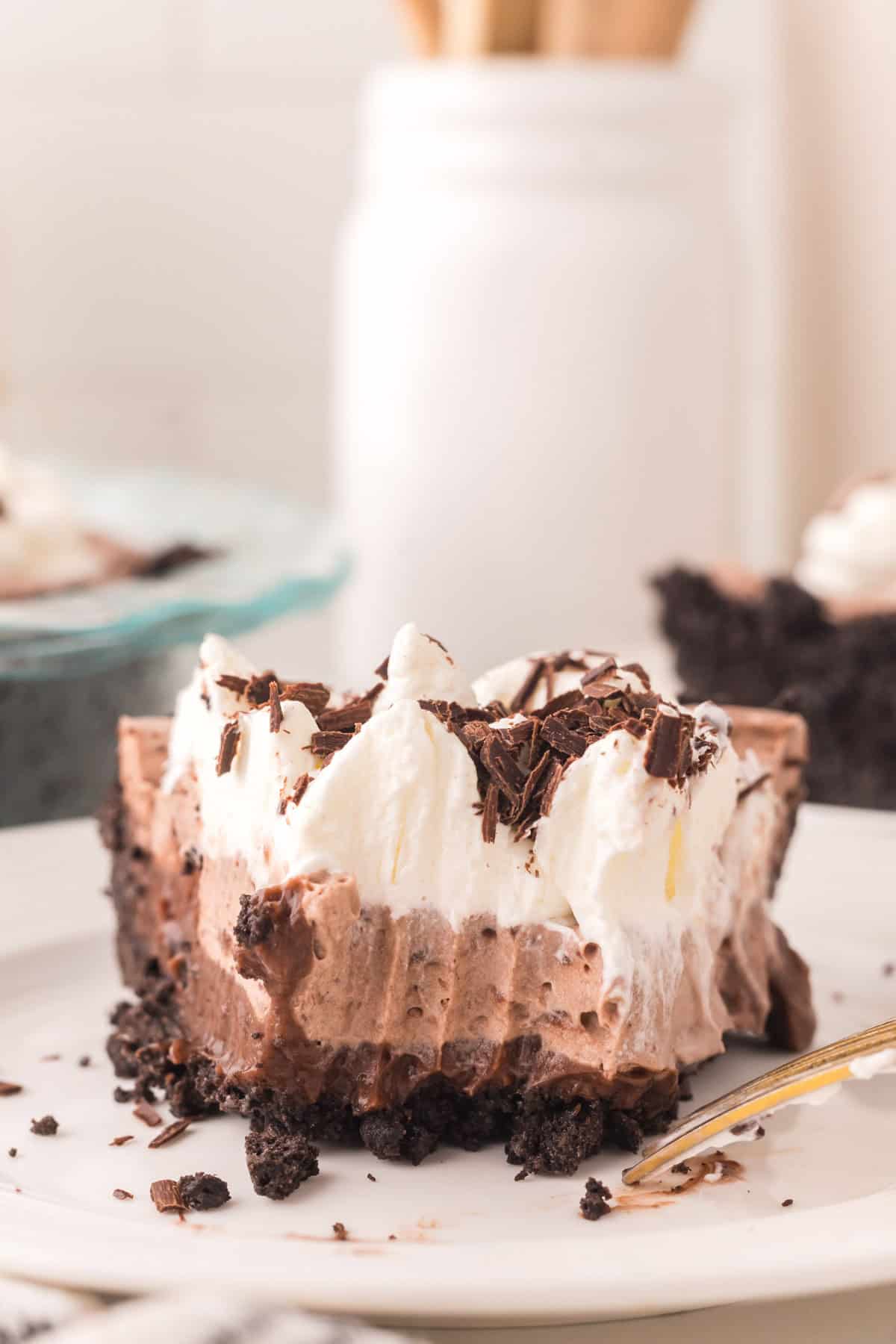 one slice of chocolate cream pie on a round white plate with a fork bite out of it.