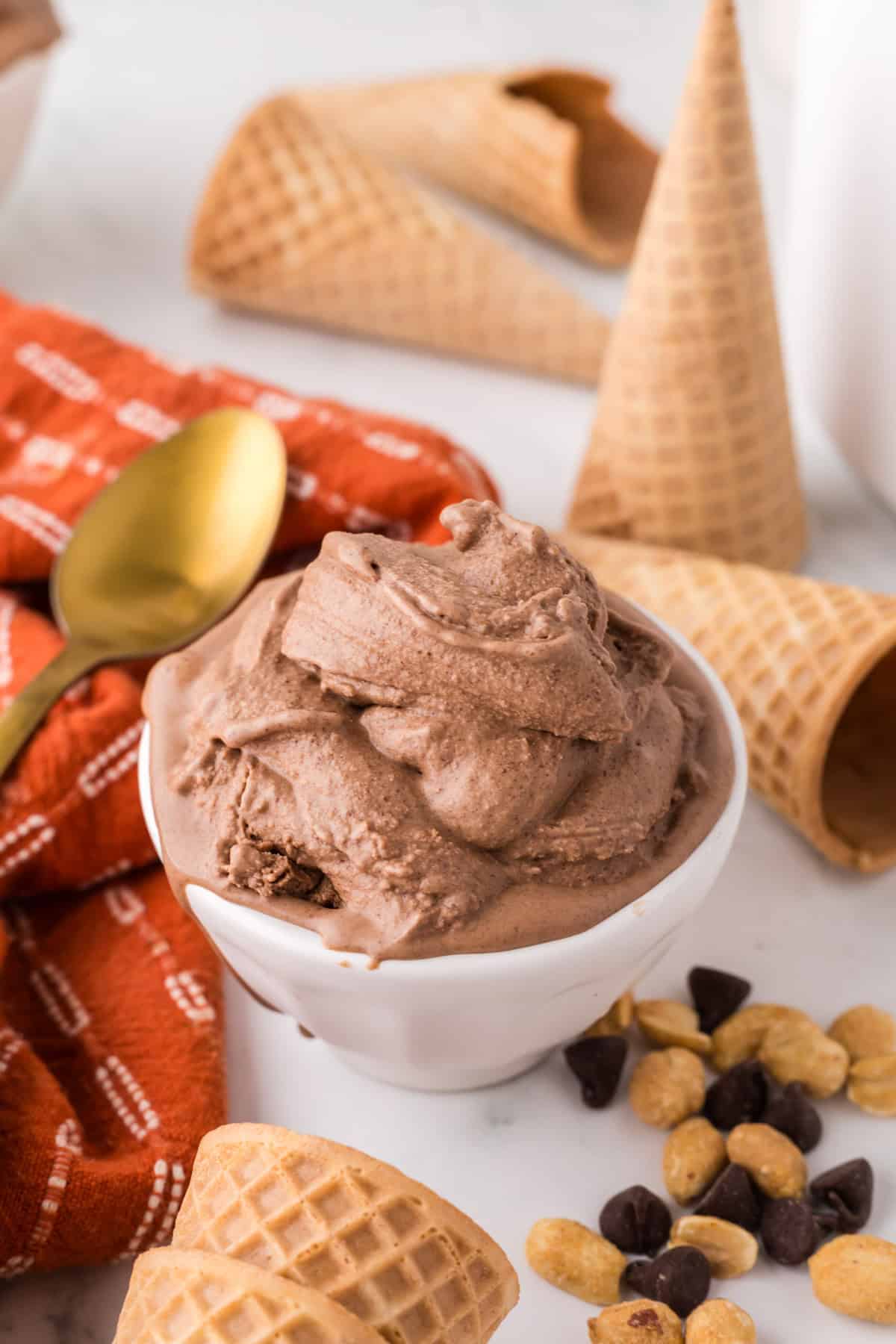 chocolate peanut butter ice cream scooped in a bowl with cones and a golden spoons around.