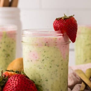 mason jar with strawberry kiwi smoothies inside and a strawberry on top.