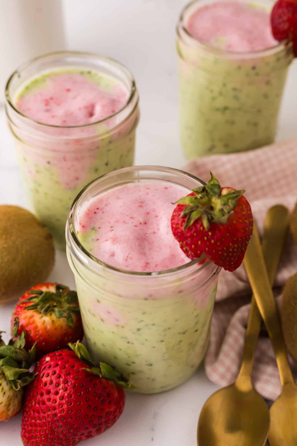 mason jar with strawberry kiwi smoothies inside and a strawberry on top.