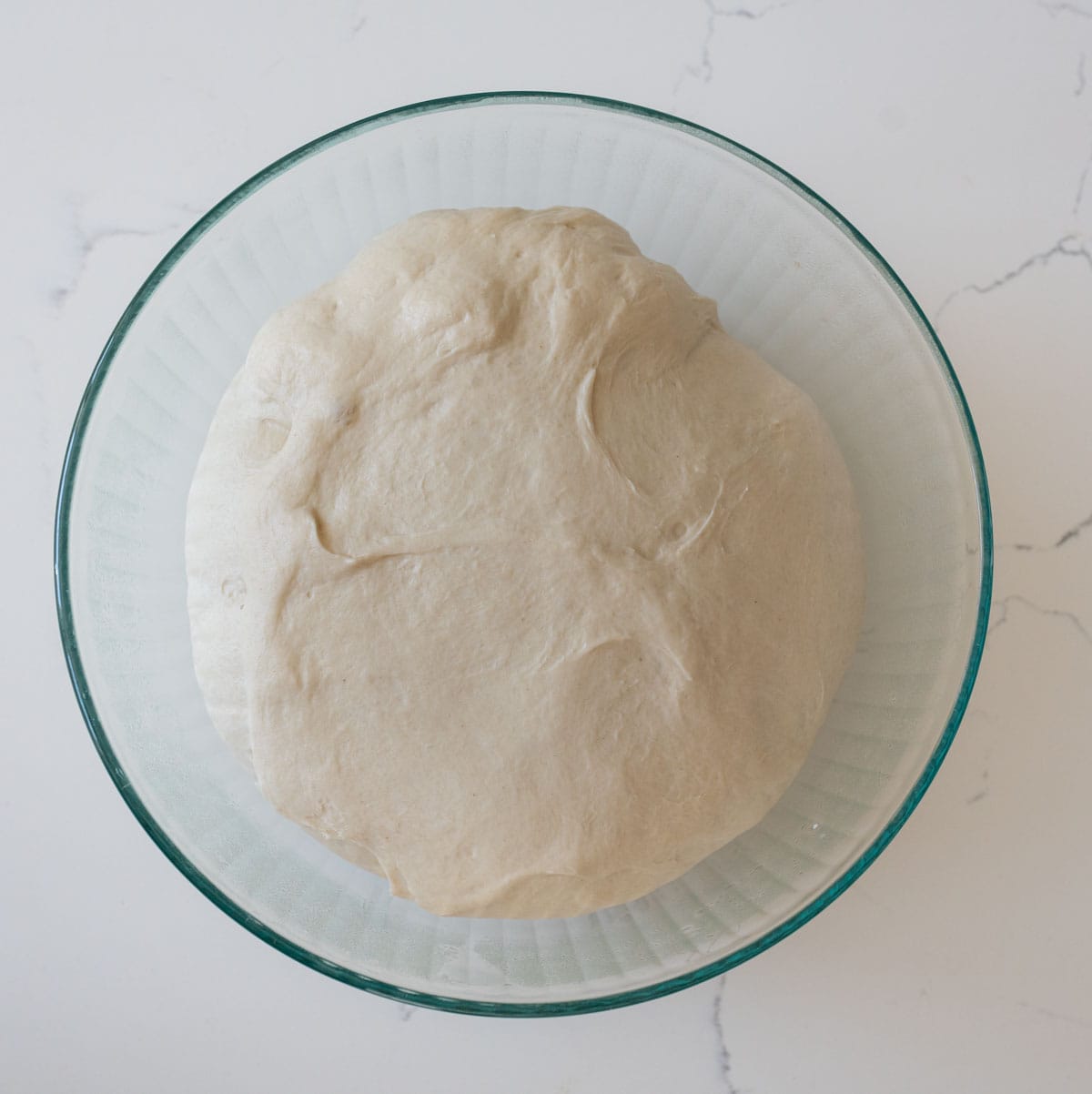 sourdough bagel dough in clear bowl on white countertop.