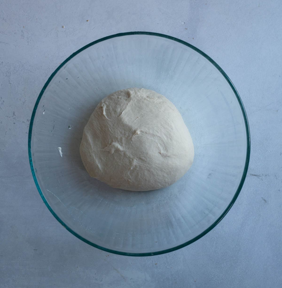 sourdough bagel dough in clear bowl on white countertop.