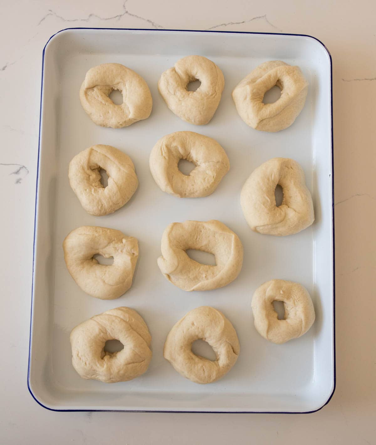 unbaked bagels on white pan on white countertop.