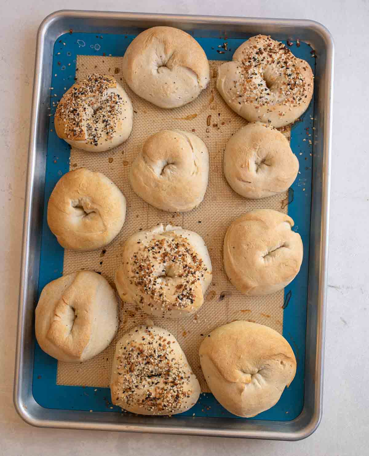 baked sourdough bagels on sheet pan on white countertop.