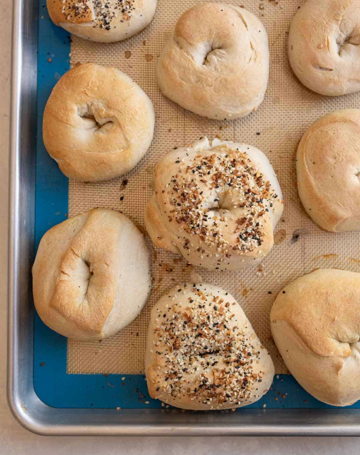 close up image of baked sourdough bagels on sheet pan.