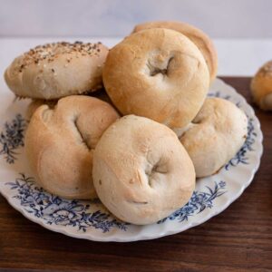 pile of baked bagels on blue and white plate on wooden countertop.