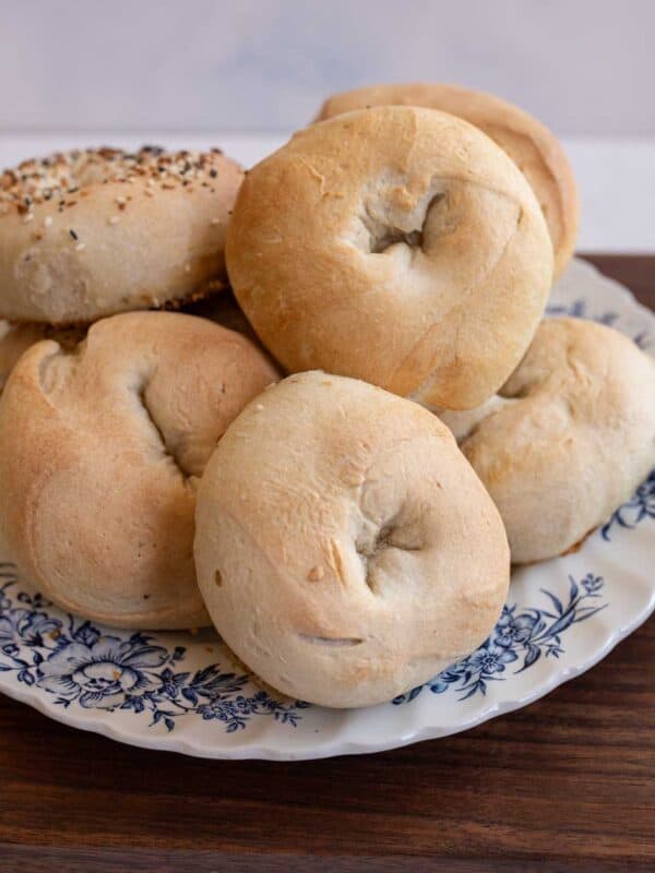 pile of baked bagels on blue and white plate on wooden countertop.