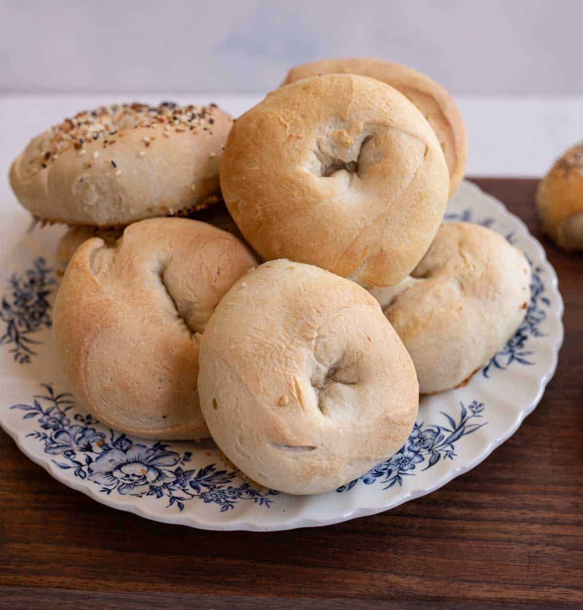 pile of baked bagels on blue and white plate on wooden countertop.