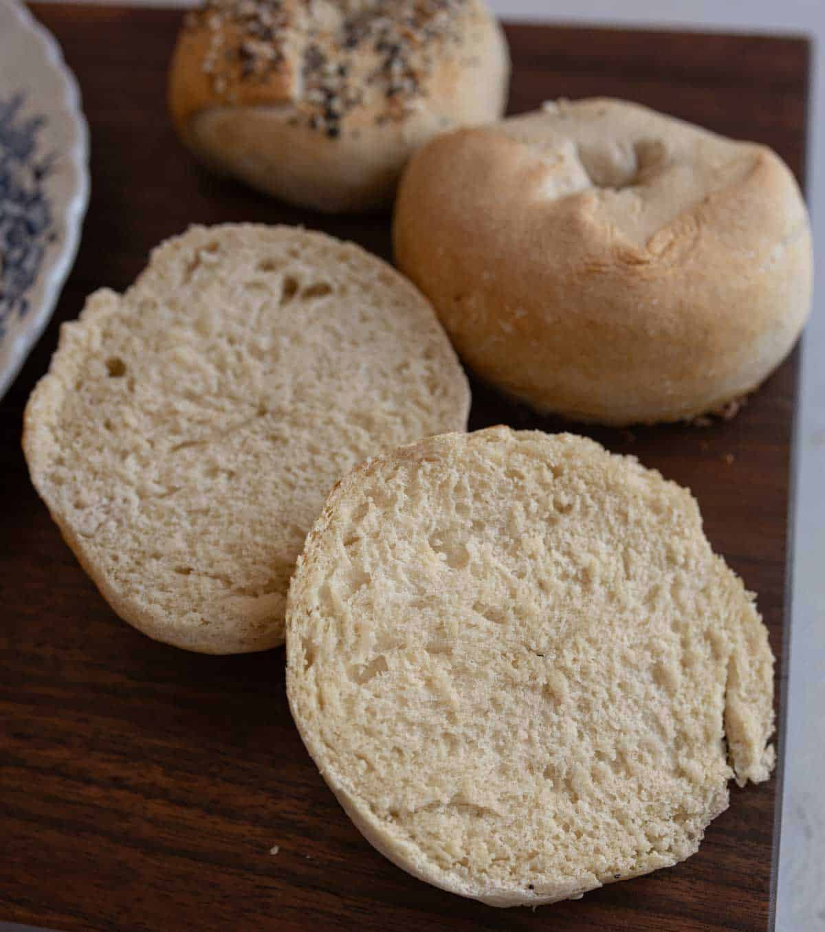 cut open bagel with two uncut bagels in background all on wood countertop.