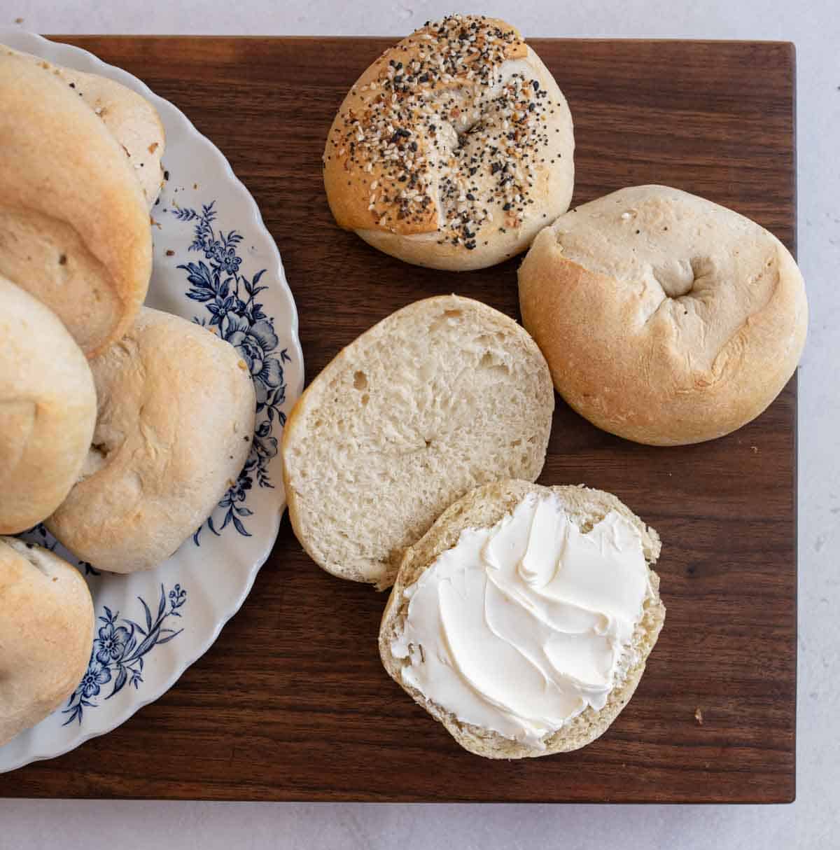 cut bagel with white cream cheese spread and other uncut bagels in background.