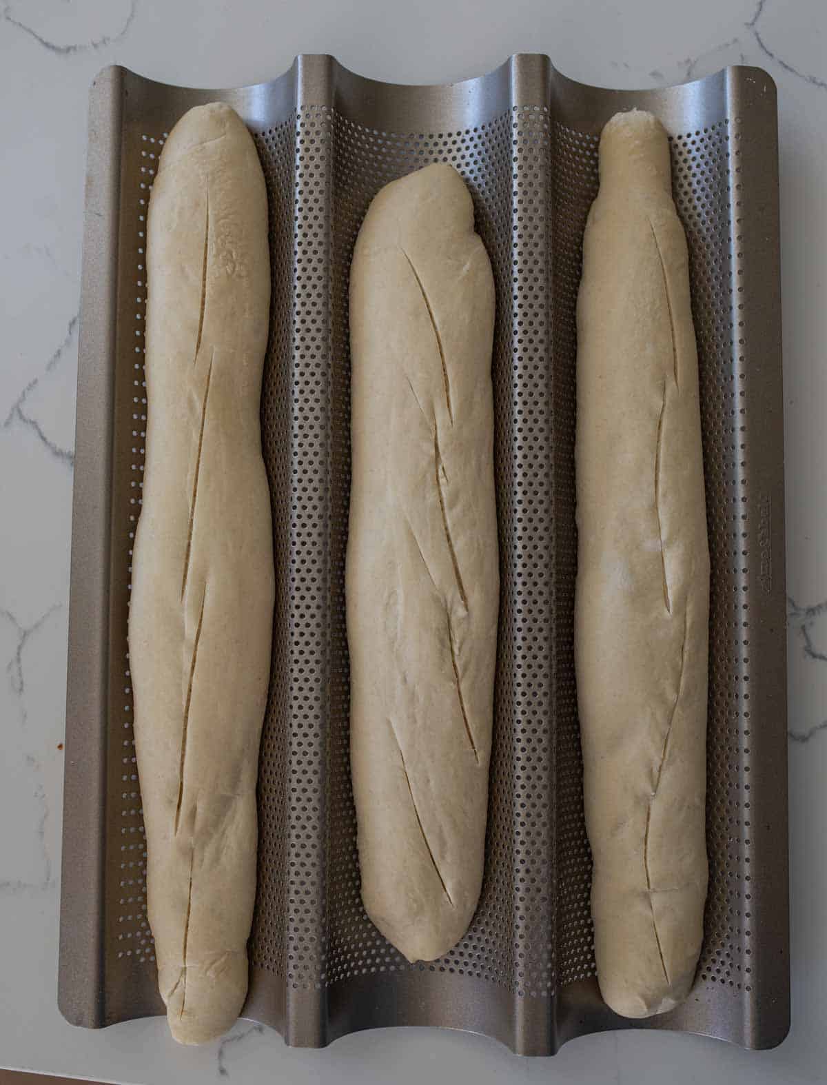 three rising pieces of dough in metal baguette pan.